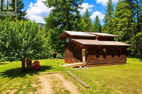 Side exterior of a rustic wooden cabin with a metal roof in a grassy yard. - 10555 Granby Road, Grand Forks