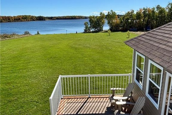 View from a deck with chairs overlooking a green lawn and water with trees. - 1056 N. Black River Road, Black River Bridge