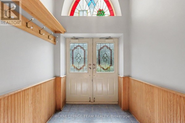 Interior entryway with double glass doors, wood-paneled walls, and a coat rack. - 10565 Main Street, North Dundas
