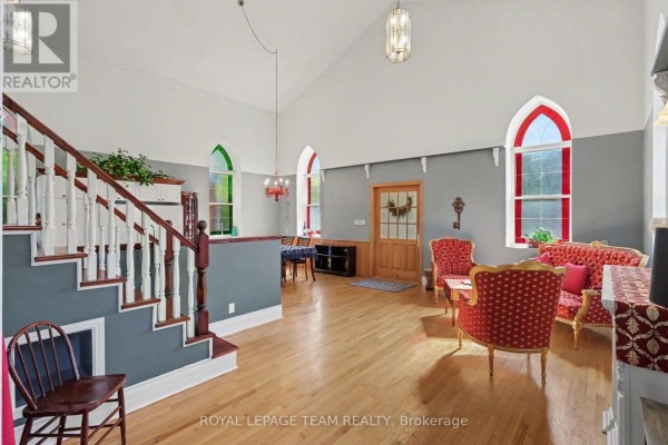 Open-concept living area with high ceilings, wood floors, a staircase, and colorful arched windows. - 10565 Main Street, North Dundas