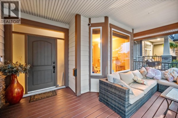 Covered front porch with wicker sofa and view of the dark wood front door. - 10574 239 Street, Maple Ridge
