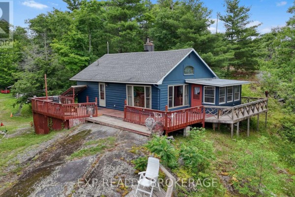 Red front door and window on a blue sided house with a wooden deck. - 1058 Perry Road, Frontenac