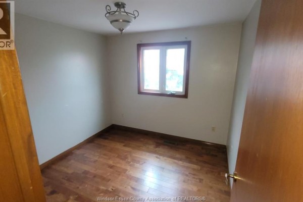 Bedroom with light grey walls, wood flooring, and a wooden window frame. - 1058 Riverdale, Windsor