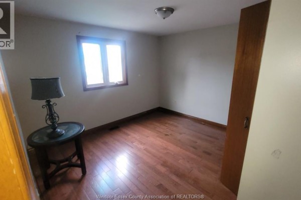 Bedroom with light grey walls, wood flooring, and a decorative lamp on a side table. - 1058 Riverdale, Windsor