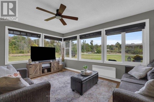 Living area with grey sofas, large windows, and a rustic TV stand. - 1058 Sunrise Drive, Ramara