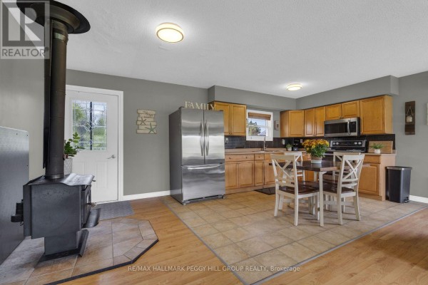 Kitchen with stainless steel appliances, wooden cabinets, dining table, and wood stove. - 1058 Sunrise Drive, Ramara