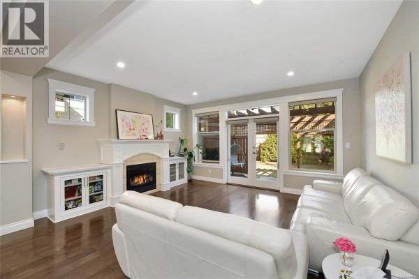 Living room with a gas fireplace, white sofas, dark hardwood floors, and glass doors to the backyard. - 1059 Clare St, Victoria