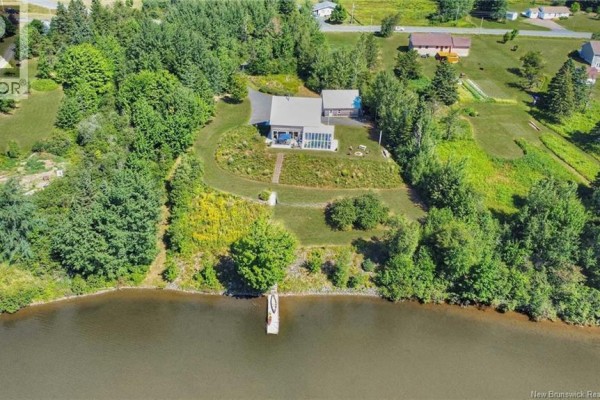 Aerial view of the property from the water, showing the house, outbuildings, and surrounding trees. - 1059 Nb-365, Gauvreau