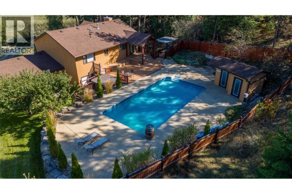 Aerial view of a house with an in-ground swimming pool, wooden deck, and backyard sheds. - 10590 Long Road, Lake Country