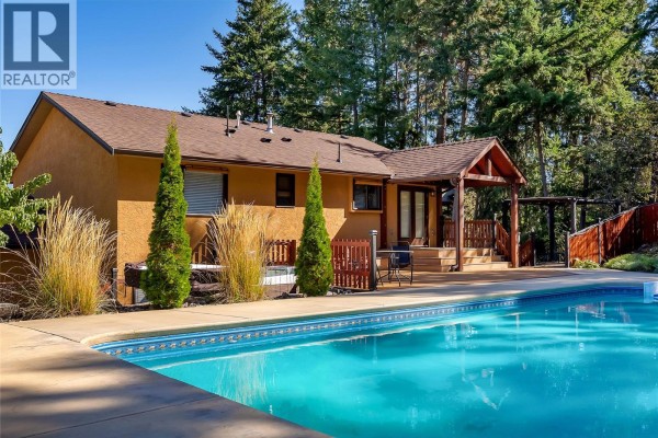 View of the house exterior, pool, and deck with tall grasses and trees. - 10590 Long Road, Lake Country