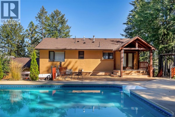 View of the house exterior, pool, and deck with tall grasses and trees. - 10590 Long Road, Lake Country