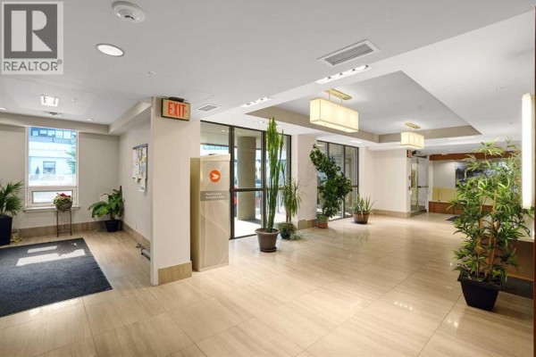 Apartment building lobby with glass doors, tile floors, and potted plants. - 106, 10 Shawnee Hill Sw, Calgary