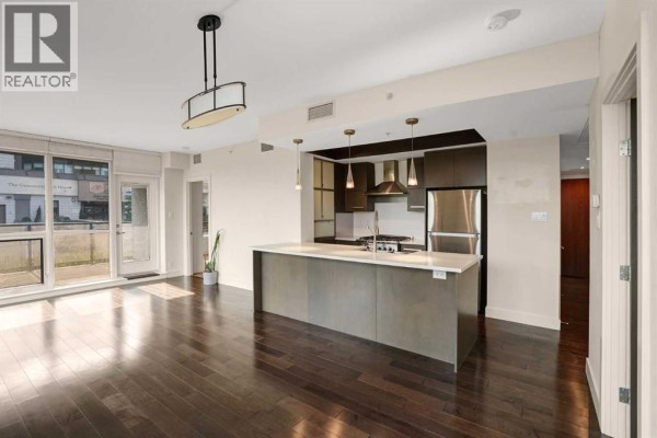 Open concept living area and kitchen with a large island and dark hardwood floors. - 106, 10 Shawnee Hill Sw, Calgary