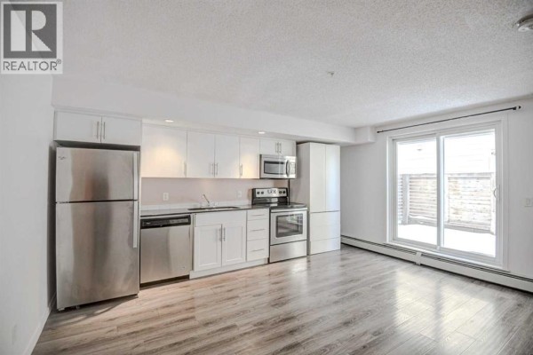 Studio apartment kitchen with white cabinets, stainless steel appliances, and a sliding glass door. - 106, 1920 11 Avenue Sw, Calgary
