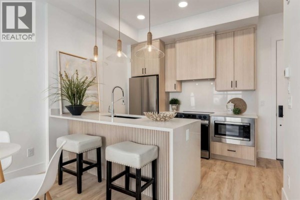 Modern kitchen with light wood cabinets, white quartz countertops, stainless steel appliances, and island seating. - 106, 330 Dieppe Drive Sw, Calgary
