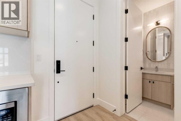 Interior view of a hallway with a white door, coat closet, and a small powder room with a vanity. - 106, 330 Dieppe Drive Sw, Calgary