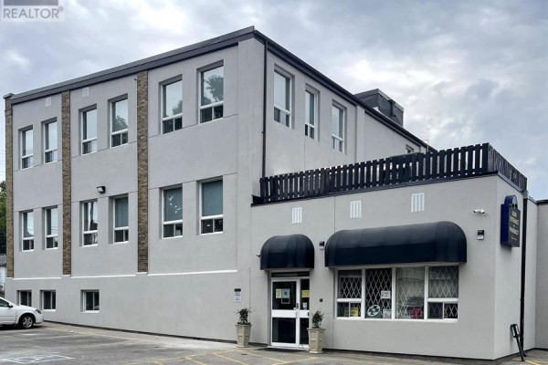 Exterior view of a two-story commercial building with light grey stucco and black trim. - 106 - 21 Surrey Street W, Guelph