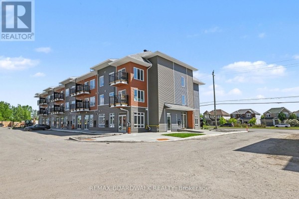 Side view of a three-story commercial building with gray and red siding, glass storefronts, and balconies. - 106 - 2370 Tenth Line Road, Ottawa