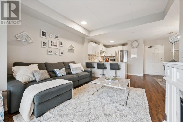 Living room with sofa, fireplace, TV, and large sliding glass doors to balcony. - 106 - 7 Kay Crescent, Guelph