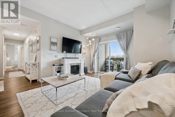 Living room with view of kitchen, dining area, and fireplace with television above. - 106 - 7 Kay Crescent, Guelph