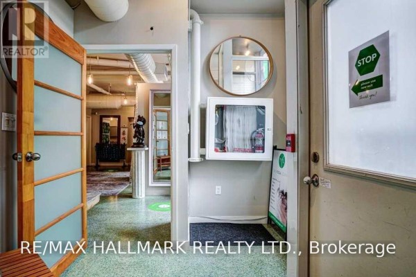 Interior view of a hallway with polished concrete floors, wooden doors, exposed pipes, and a circular mirror. - 106 - 80 Sherbourne Street, Toronto