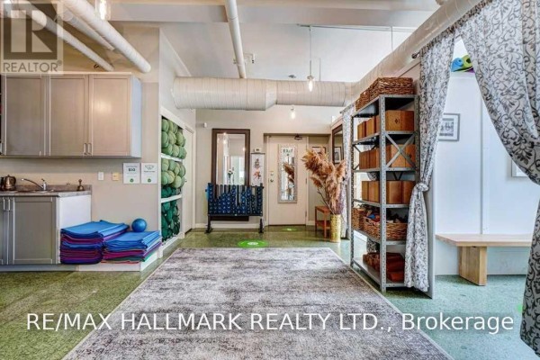 A spacious room with high ceilings, exposed ductwork, yoga mats, storage shelves, and a patterned rug. - 106 - 80 Sherbourne Street, Toronto