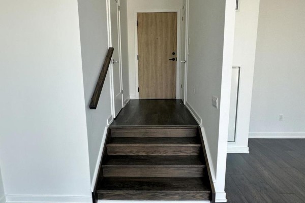 Dark wood stairs leading to a hallway with a wood grain door. - 106 - 801 The Queensway, Toronto