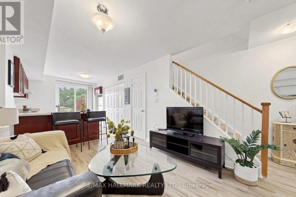 Living room with hardwood floors, white staircase, leather sofa, glass coffee table, and TV. - 106 - 870 Jane Street, Toronto