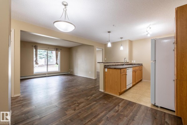 Open concept living room and kitchen with dark wood floors and wood cabinets. - #106 1188 Hyndman Rd Nw, Edmonton