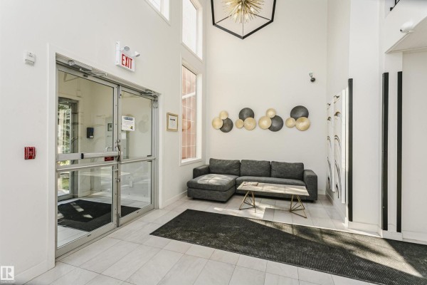 Apartment building lobby with a grey sectional sofa, marble tile floor, and tall ceilings. - #106 12110 106 Av Nw, Edmonton