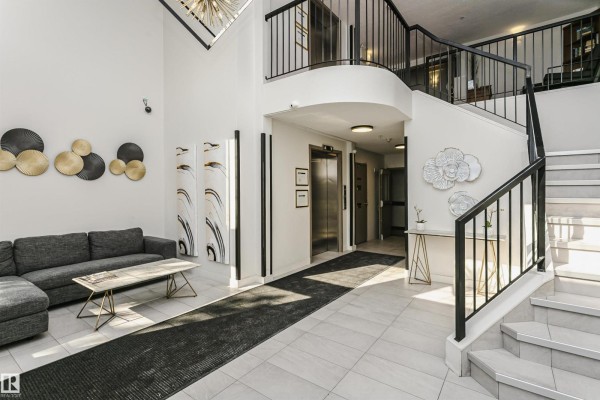Apartment building lobby with a sofa, elevator, staircase, and decorative wall art. - #106 12110 106 Av Nw, Edmonton