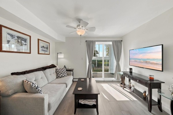 Living room with a grey sofa, coffee table, television, and sliding glass doors. - 106 14881 Marine Drive, White Rock