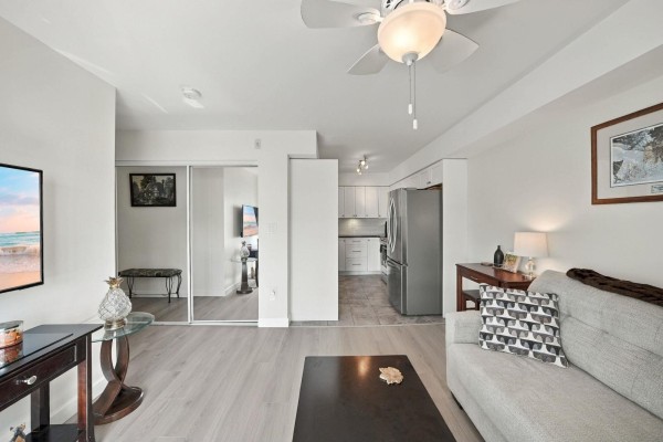 Living room and kitchen area with stainless steel appliances, light grey flooring, and sliding doors. - 106 14881 Marine Drive, White Rock