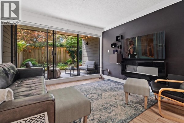 Living room with a dark leather sofa, fireplace, large television, and sliding glass doors to the patio. - 106 1710 W 13th Avenue, Vancouver