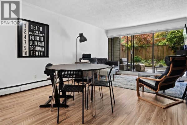 Dining area with a round black table and chairs, and a view of the living room and patio. - 106 1710 W 13th Avenue, Vancouver