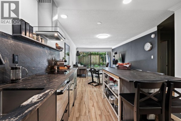 Kitchen featuring dark wood cabinets, granite countertops, stainless steel appliances, and an island with seating. - 106 1710 W 13th Avenue, Vancouver
