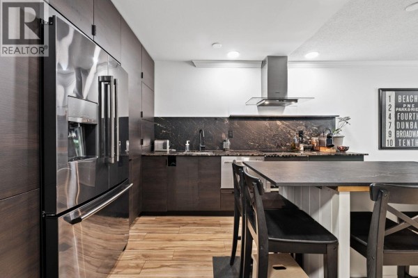 Modern kitchen with a large stainless steel refrigerator, dark wood cabinetry, and a granite-topped island. - 106 1710 W 13th Avenue, Vancouver