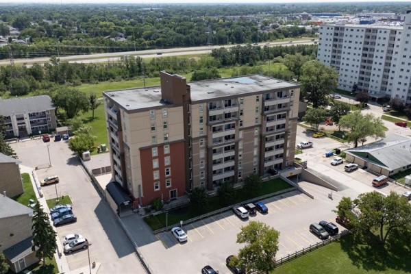 Aerial perspective of the apartment building and surrounding parking area under a bright sky. - 106 180 Beliveau Road, Winnipeg