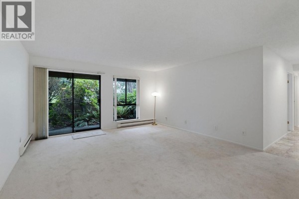 Empty living room with beige carpet, sliding glass doors, and a single window overlooking greenery. - 106 333 Wethersfield Drive, Vancouver