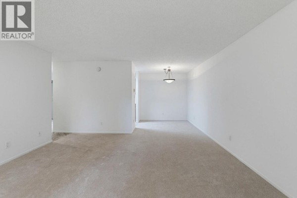 Wide view of an empty apartment living and dining area with light beige carpet and white walls. - 106 333 Wethersfield Drive, Vancouver