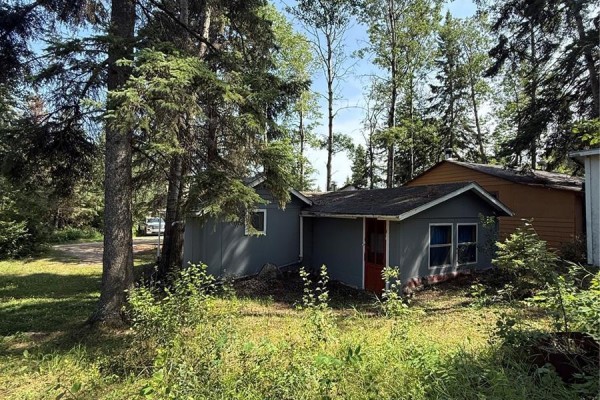 Rear view of the grey cottage, partially obscured by trees and foliage. - 106 Agnes Street, Emma Lake