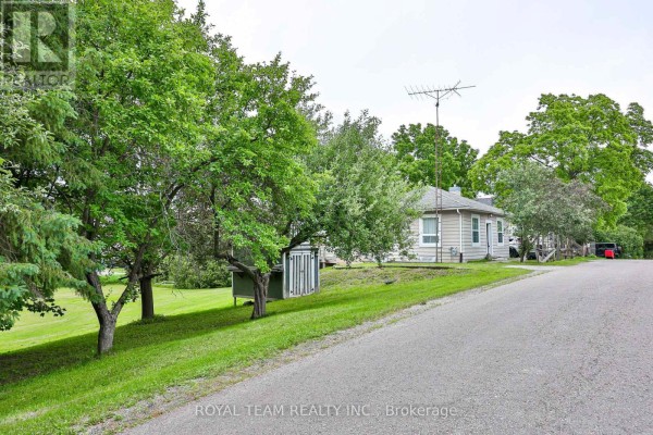 A light-colored house with white trim and a small shed sits on a grassy slope with mature trees. - 106 Centre Street, King