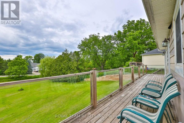 Wooden deck with glass railings overlooking a green lawn and treed landscape under a cloudy sky. - 106 Centre Street, King
