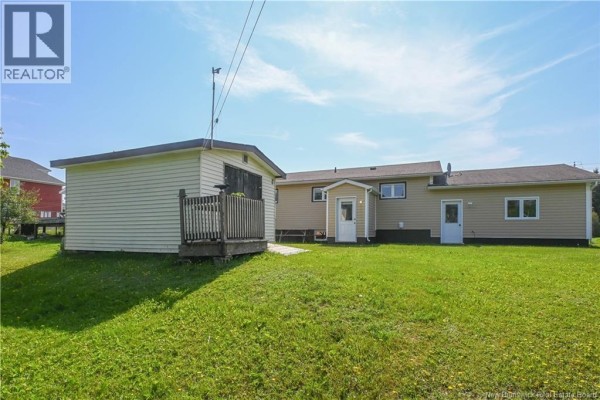 Kitchen with white cabinets, stainless steel refrigerator, island with seating, and sink. - 106 Des Champs Street, Lameque