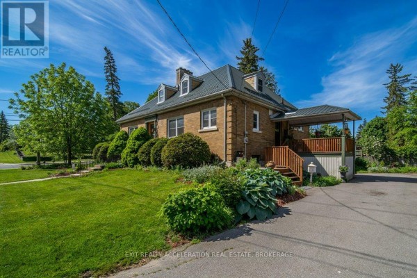 Side view of brick house with green roof, wooden deck, and surrounding greenery. - 106 Donald Street, Greater Napanee