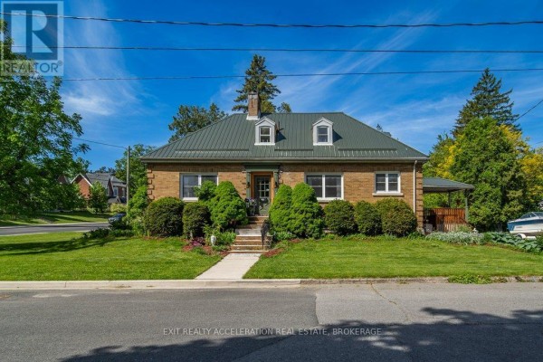 Front exterior of a brick bungalow with a green metal roof and arched entryway. - 106 Donald Street, Greater Napanee