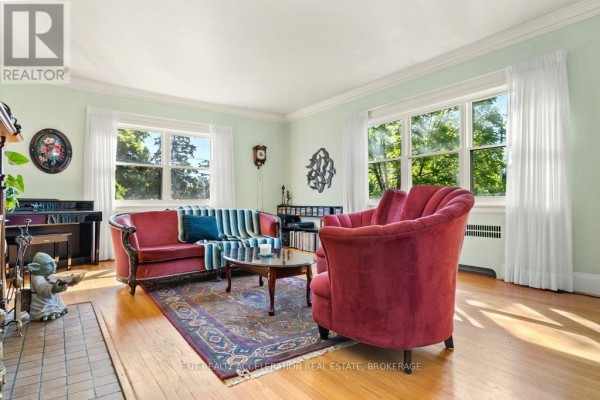 Living room with light green walls, red velvet sofa and armchair, and hardwood floors. - 106 Donald Street, Greater Napanee