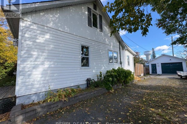 Side view of the white vinyl-sided house showing a driveway and garage with a water tower in the background. - 106 Fifteenth Avenue, Cochrane