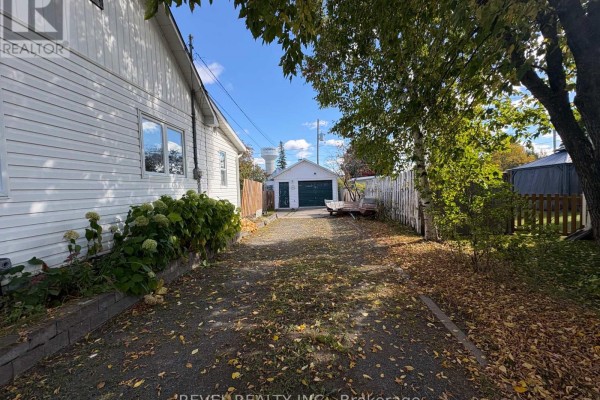 View of the driveway leading to the detached garage, bordered by a wooden fence and autumn trees. - 106 Fifteenth Avenue, Cochrane