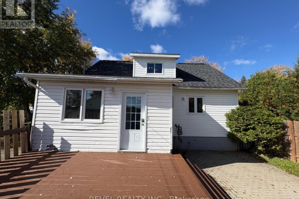 Rear exterior view of the house with a wooden deck and a paved patio area. - 106 Fifteenth Avenue, Cochrane